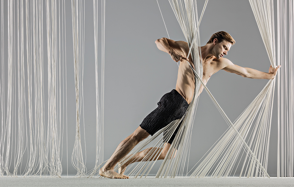 Company Dancer Brett Conway leaning forward in a wall of strings