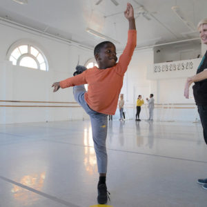 A young student in arabesque as the teacher watches