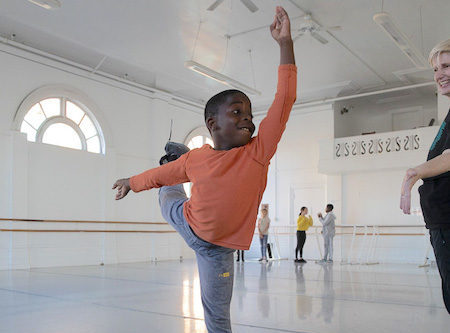A young student in arabesque as the teacher looks on