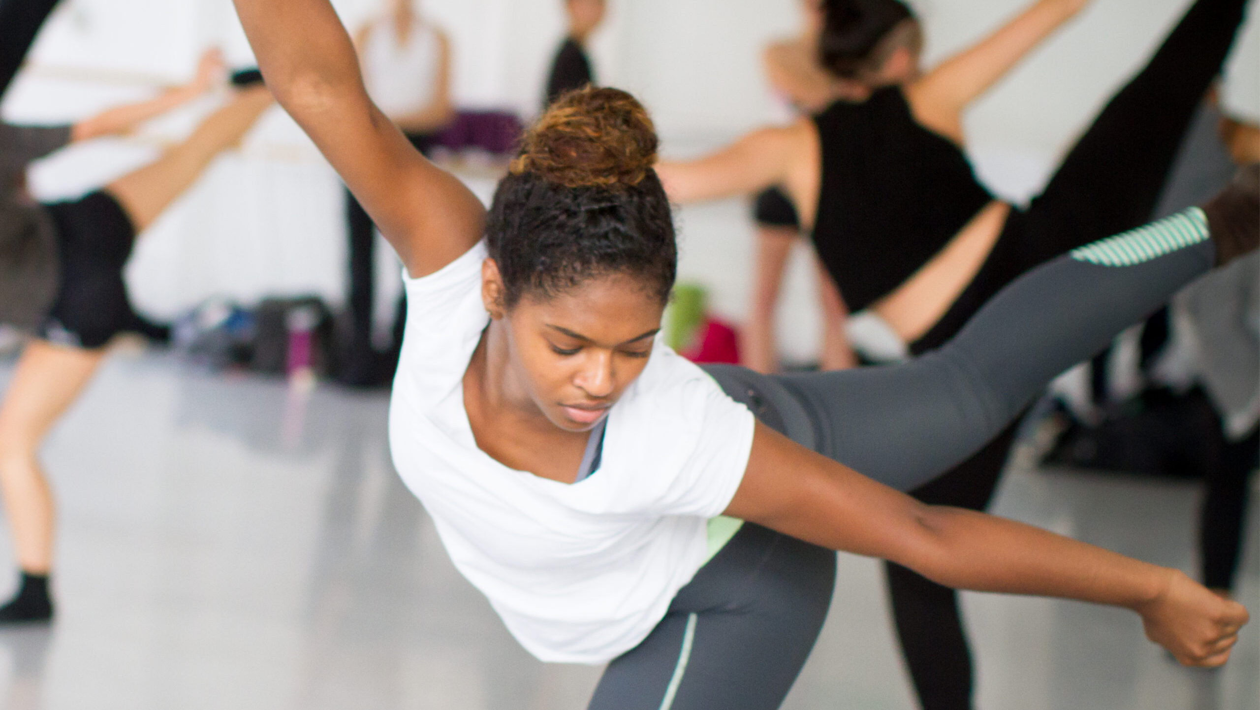 A young dancer in arabesque in a studio at LINES Dance Center with other students in the background; LINES Day imagery