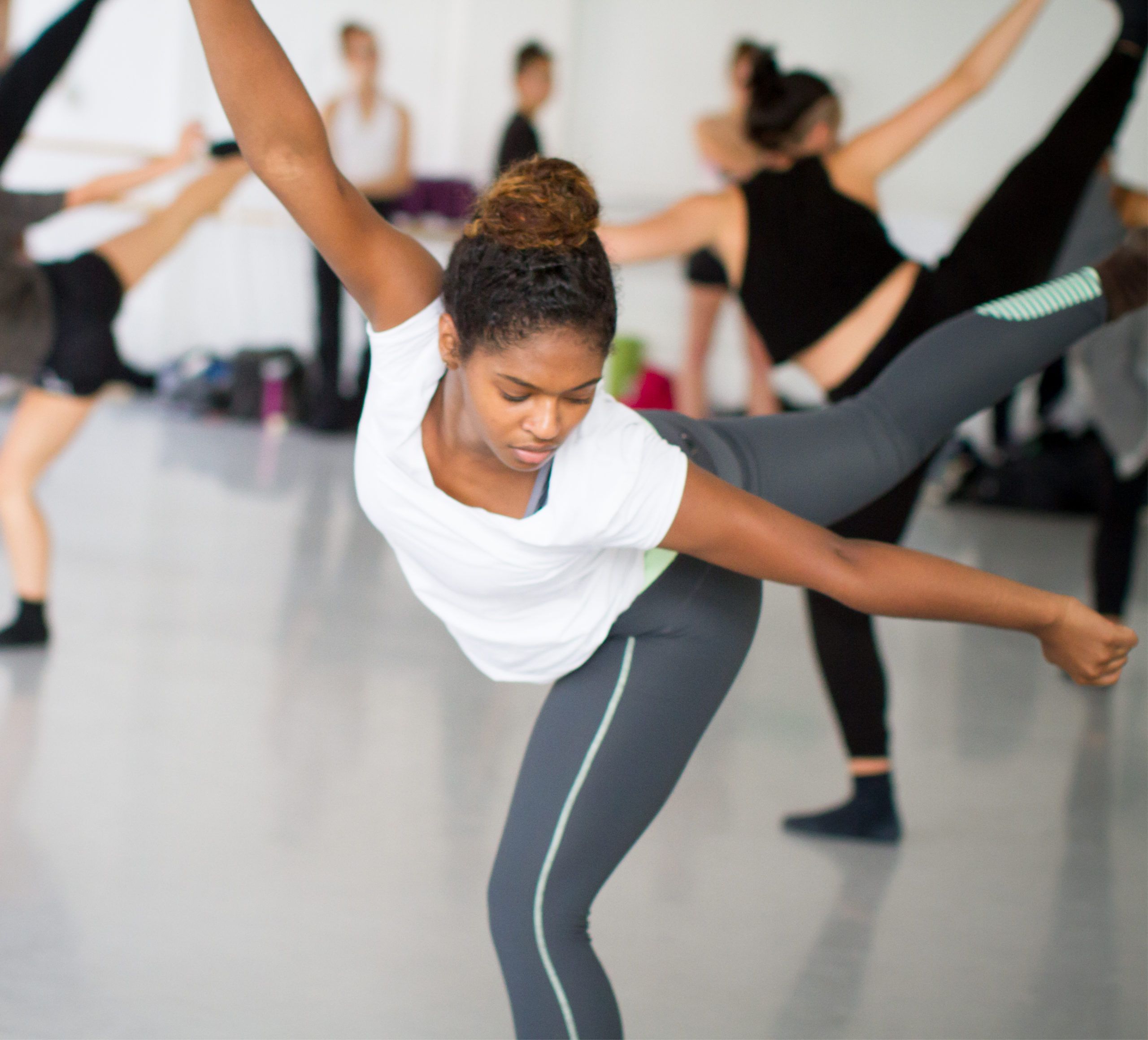 A young dancer in arabesque in a studio at LINES Dance Center with other students in the background; LINES Day imagery