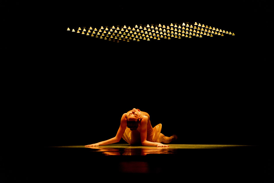 LINES Ballet company artist Madeline DeVries on the ground back arched under a light installation in Alonzo King's AZOTH