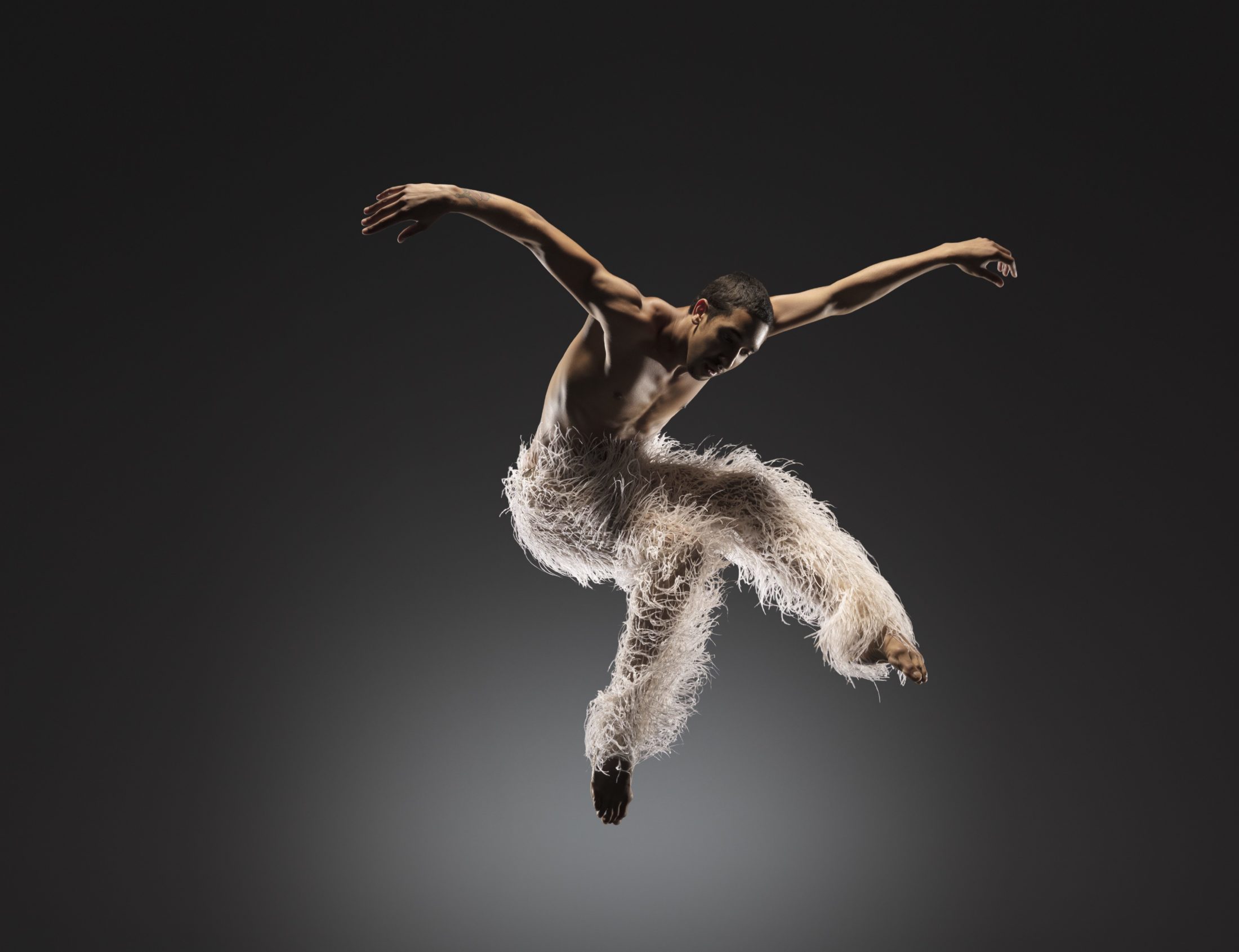 LINES Ballet company artist Shuaib Elhassan jumping against a black/gray background