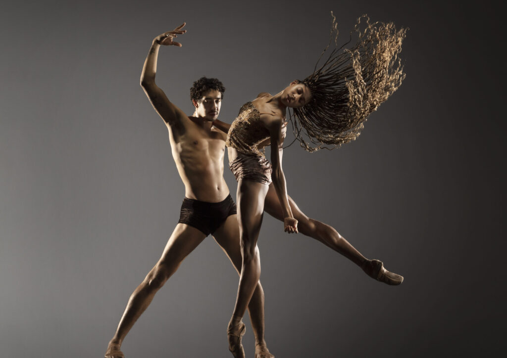 LINES Ballet company artists Adji Cissoko and Shuaib Elhassan partnering, Adji en pointe and in a demi-arabesque and Shuaib in a parallel second position with one arm around Adji's waist, the other arm pulling outward into a curved c-shape