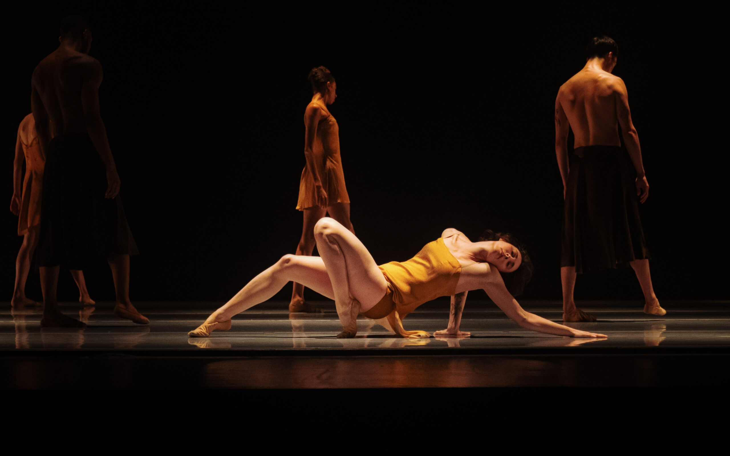 LINES Ballet company dancer Maya Harr performing floorwork in Alonzo King's "Deep River" while other company dancers walk on the stage