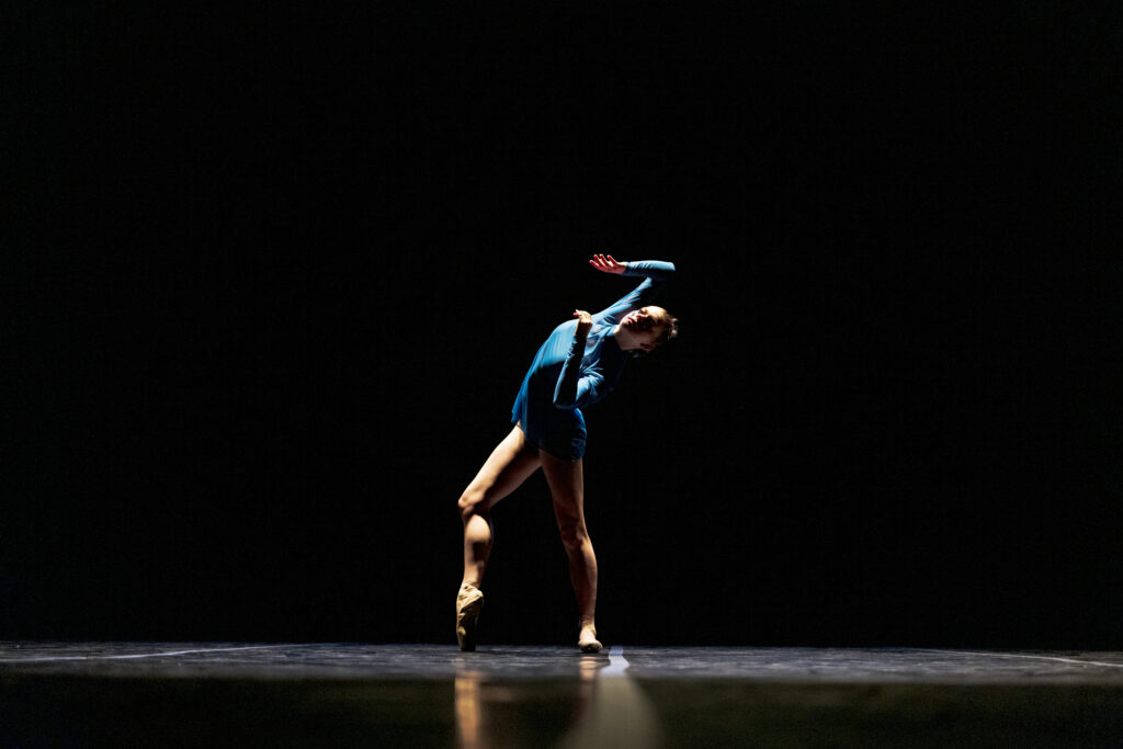 BFA at Dominican student on stage in a blue shirt pressing one foot en pointe and arching back with bent arms