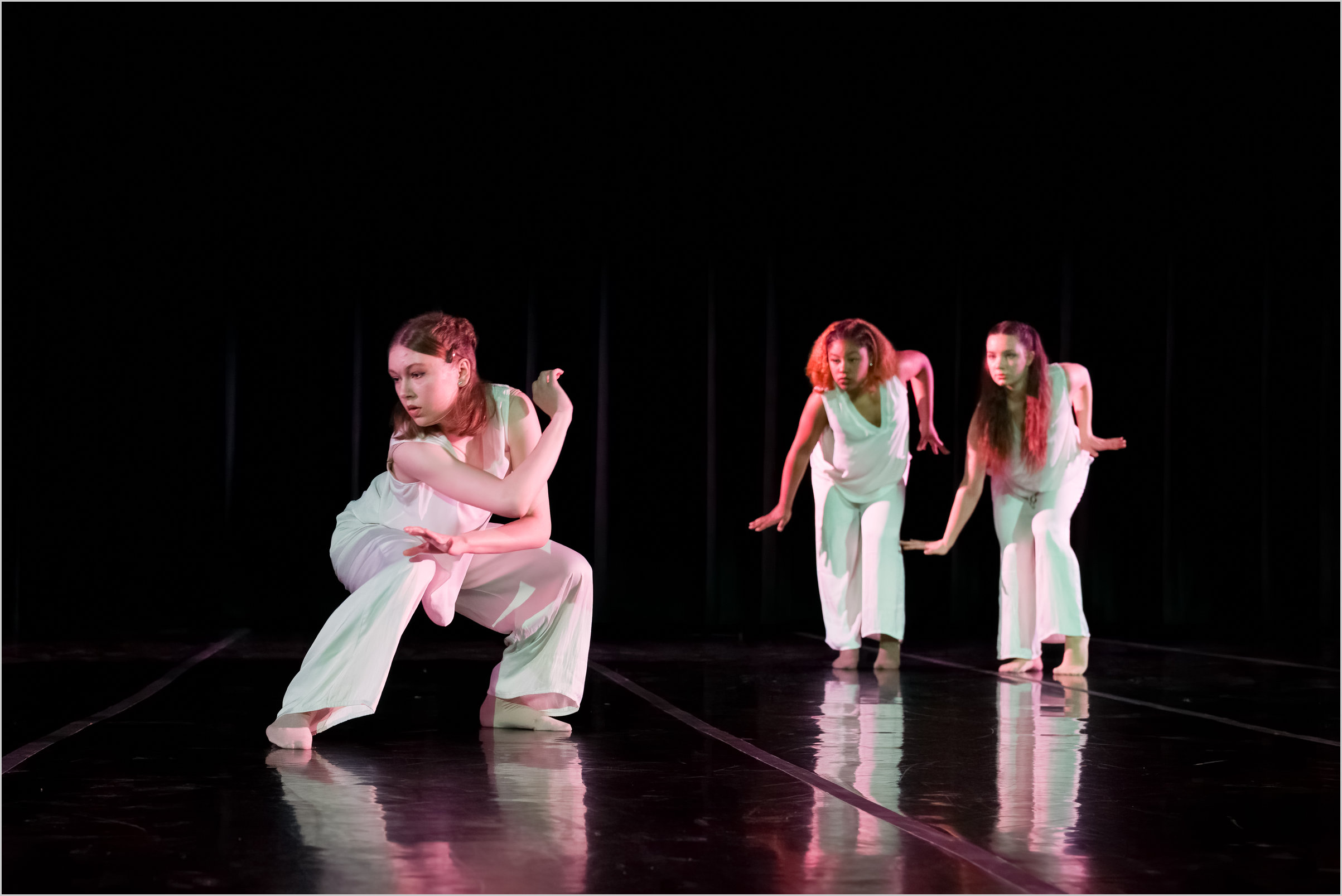 Three BFA at Dominican students dancing on stage in a showcase at Angelico Concert Hall; student artists are wearing white