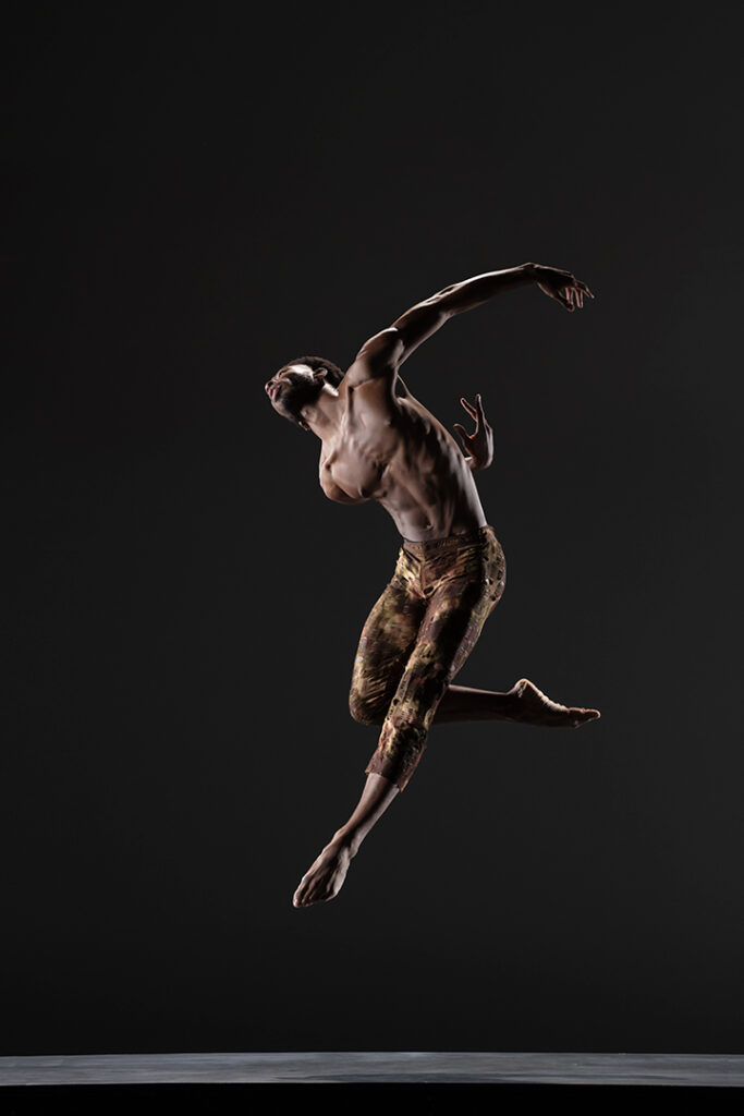 LINES Ballet Company Dancer Josh Francique jumping with one leg extended and the other bent and tucked behind