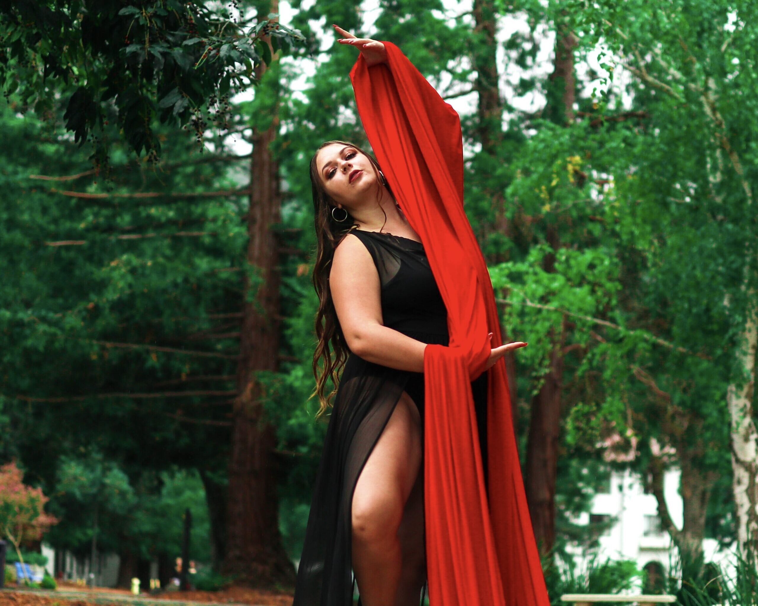 Faith Alexis dancing in a black dress holding red fabric in the woods