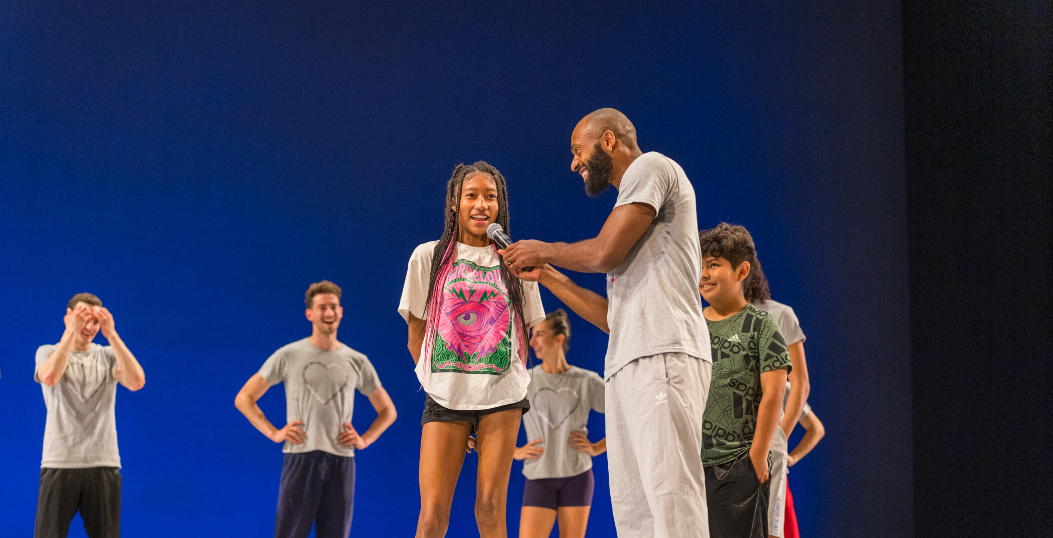 LINES Ballet company dancer Babatunji holding a microphone and talking on stage with a student at a student matinee performance; company dancers are standing behind them on stage smiling