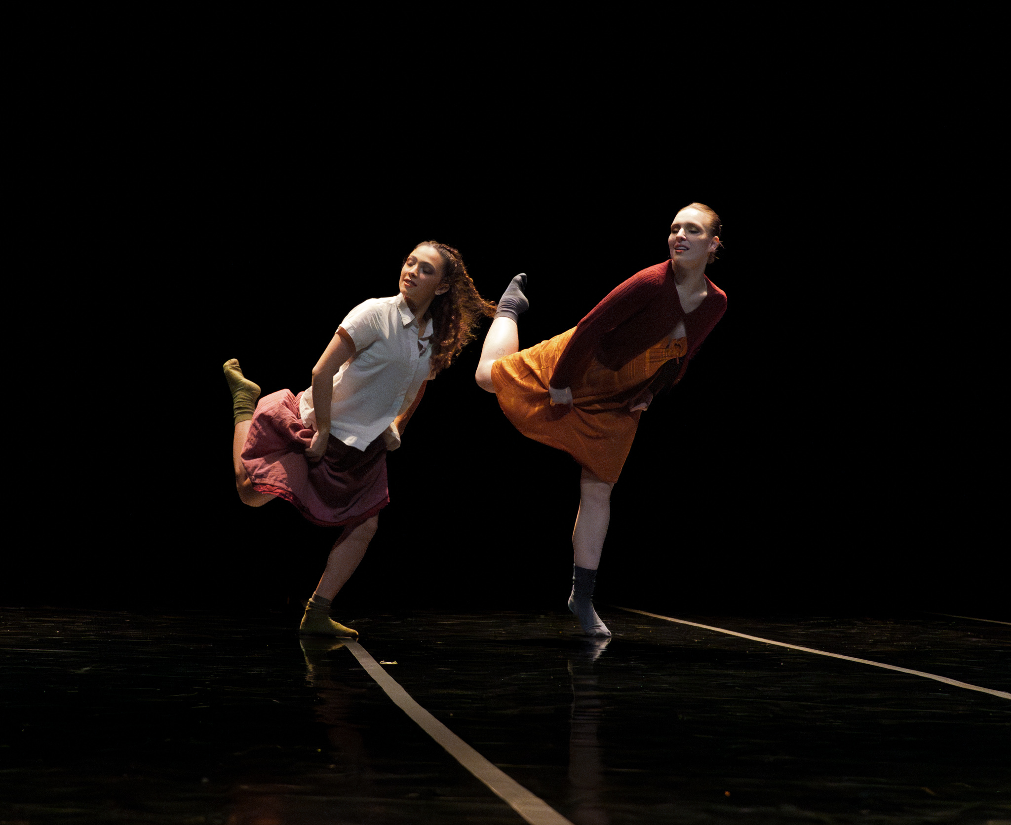 Two LINES BFA dancers in jewel colored skirts and tops lean playfully next to one another