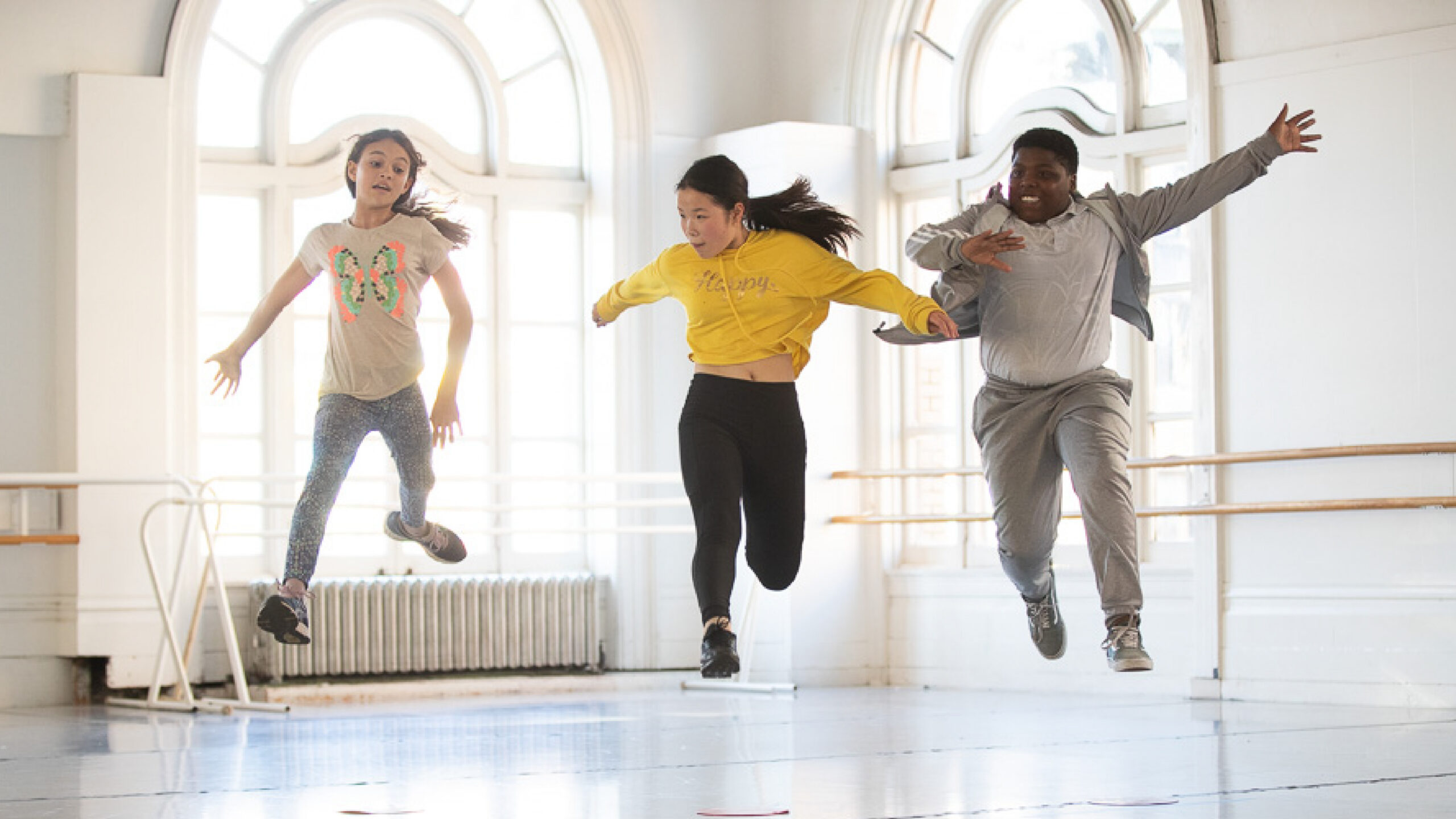 Three children jump with joy in the LINES Dance Center studios.