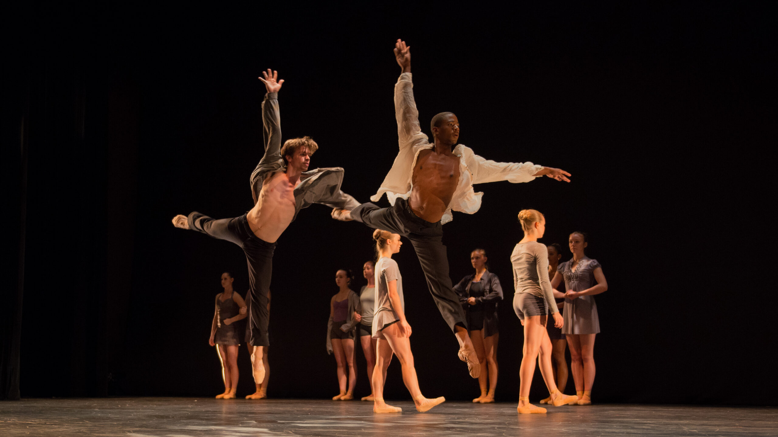Two Summer Program dancers jump simultaneously in flowy shirts.