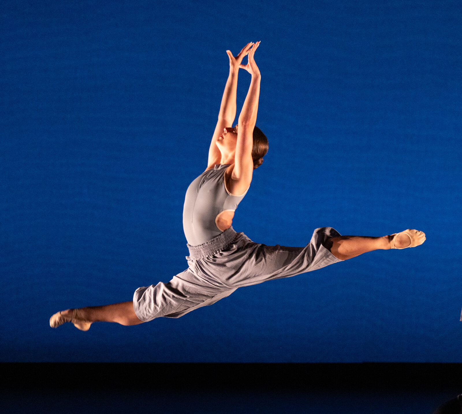 Summer Program dancer performs onstage. Dancer dressed in light blue leaps in a perfect split with dark blue backdrop.