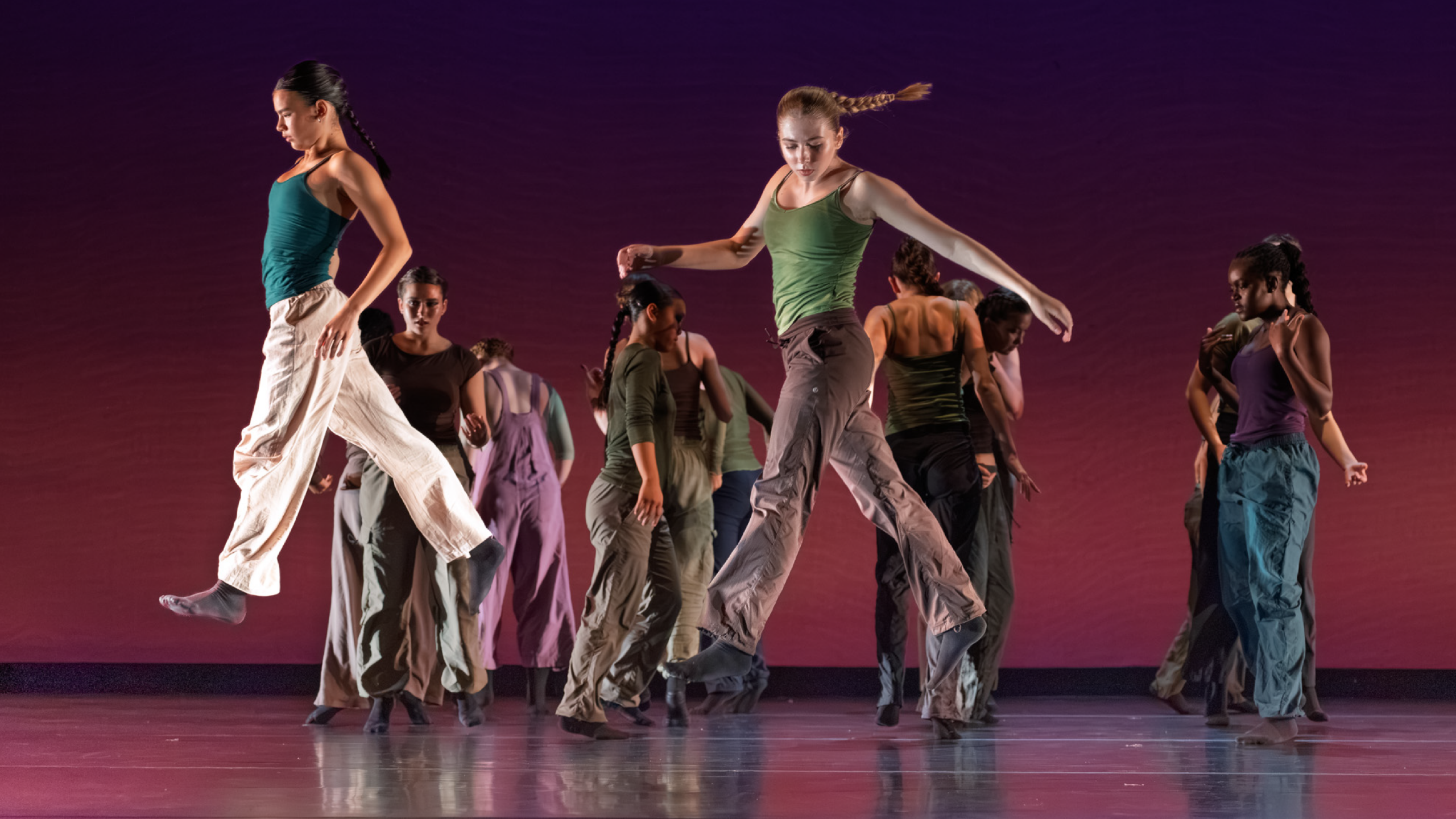 Summer Program students perform onstage. Two dancers dressed in jewel tones suspend as though walking mid-air with a group of dancers behind them.