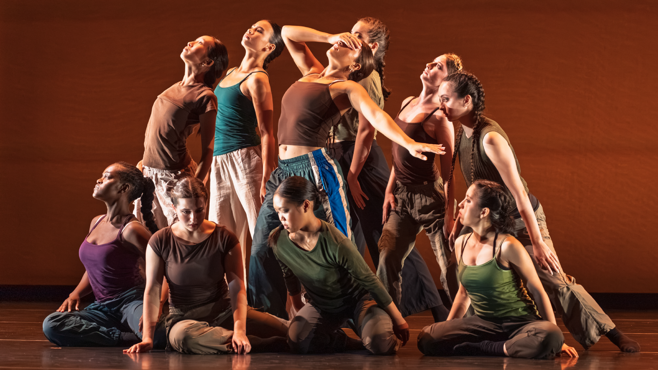 Summer Program students perform onstage. Dancers in jewel tones group together on different levels, some looking up to the sky, others down to the floor. One dancer covers their face.