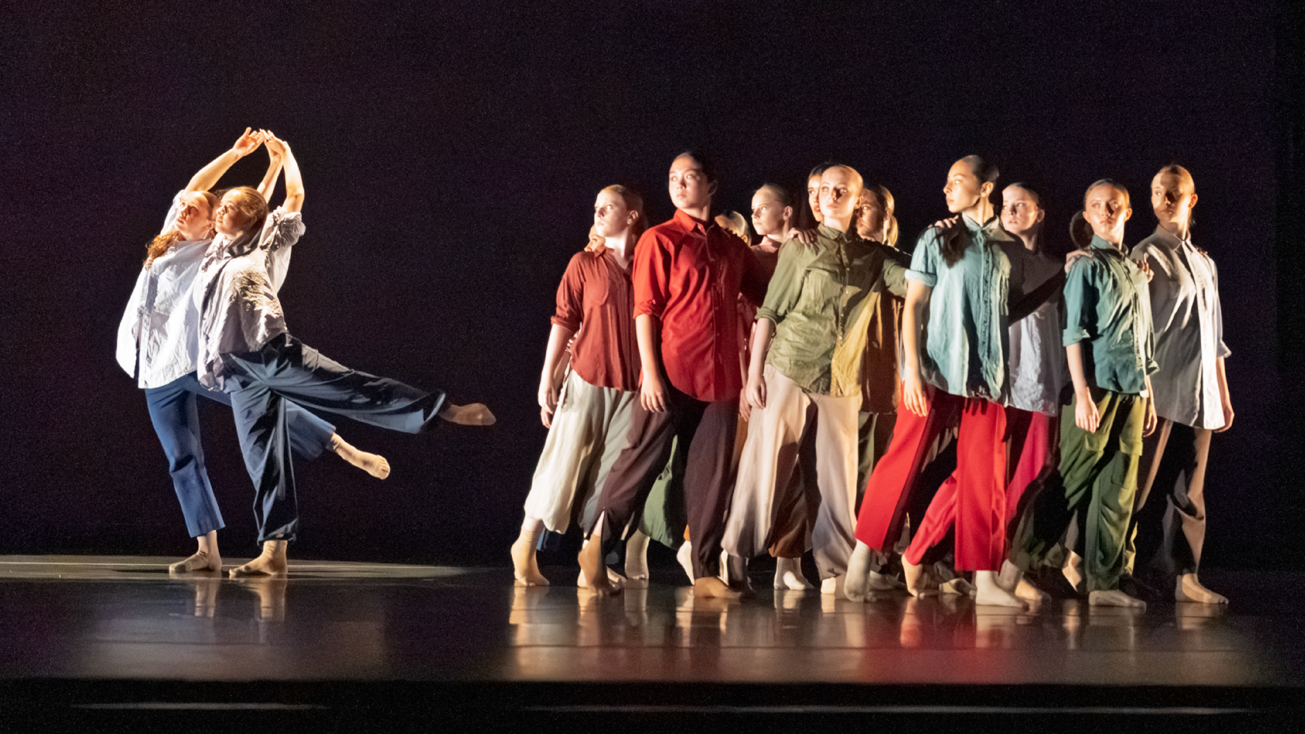 Summer Program students perform onstage. A group of dancers steps away from, while looking at two dancers reached in arabesque away from them. Dancers are in jewel tone costumes.