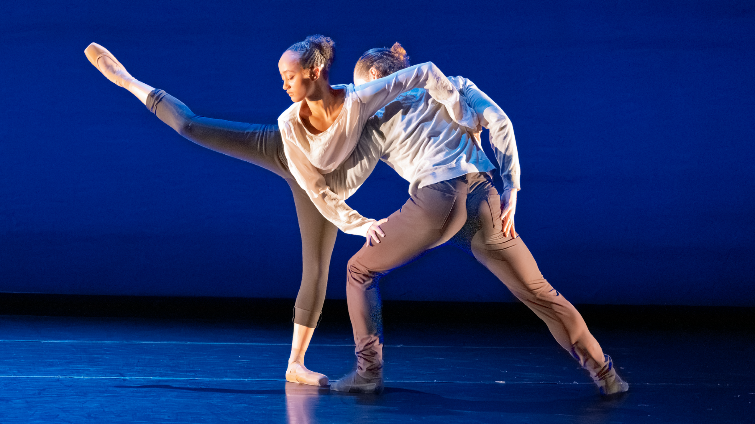 Summer Program students perform onstage. Dancers dressed in black and blue support one another, one on one leg, in front of a blue backdrop.