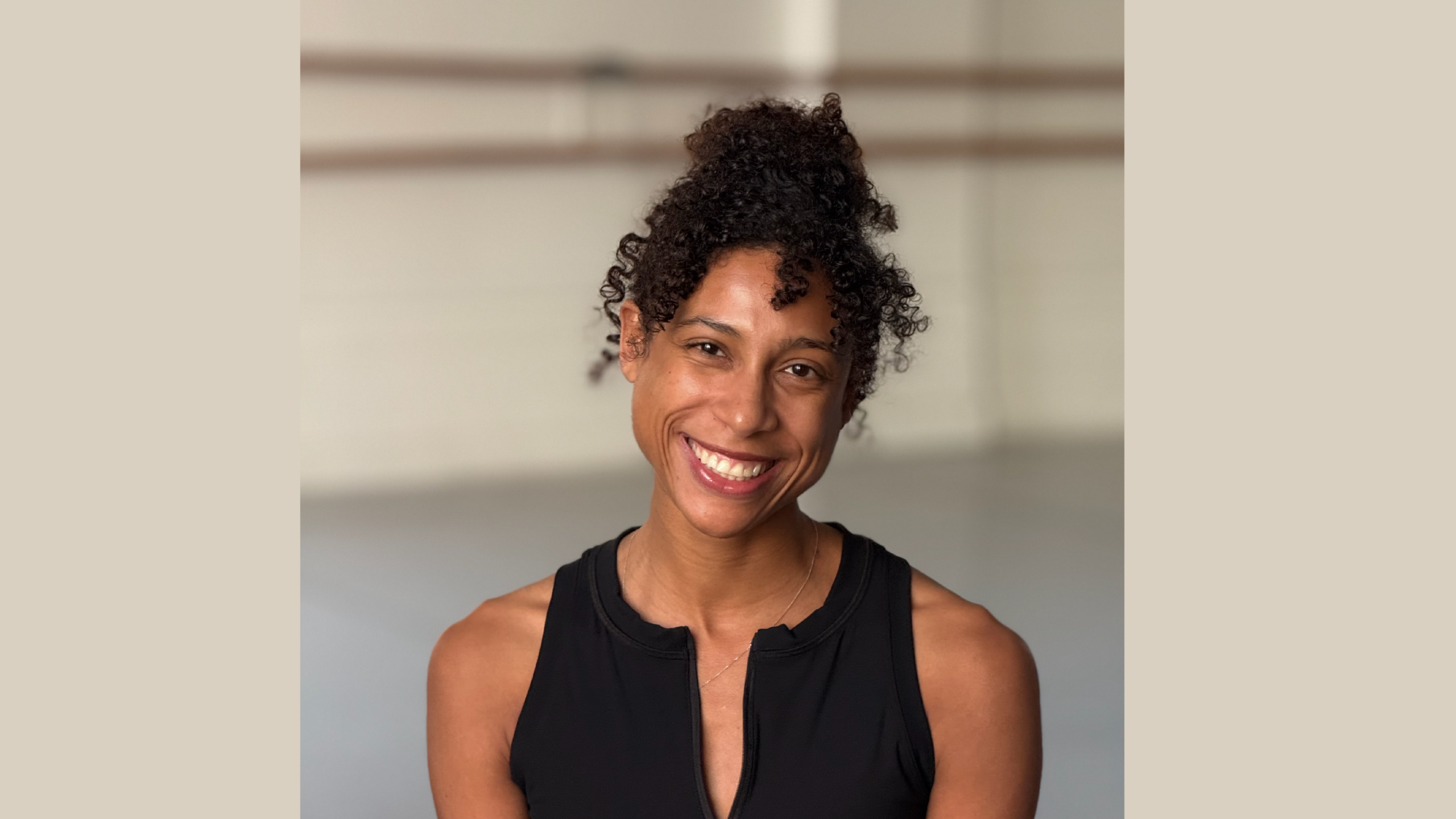 Dancer and Associate Artistic Director Adji Cissoko sits smiling at and facing the camera in LINES Ballet Studio 1.